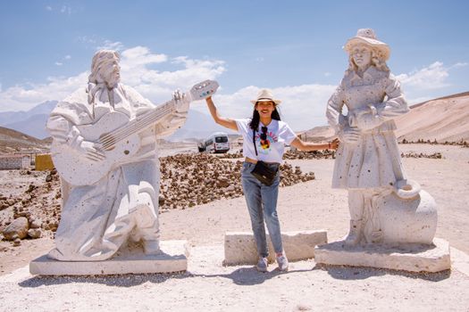 A woman stands between two large sandstone statues in the desert near Arequipa, Peru.