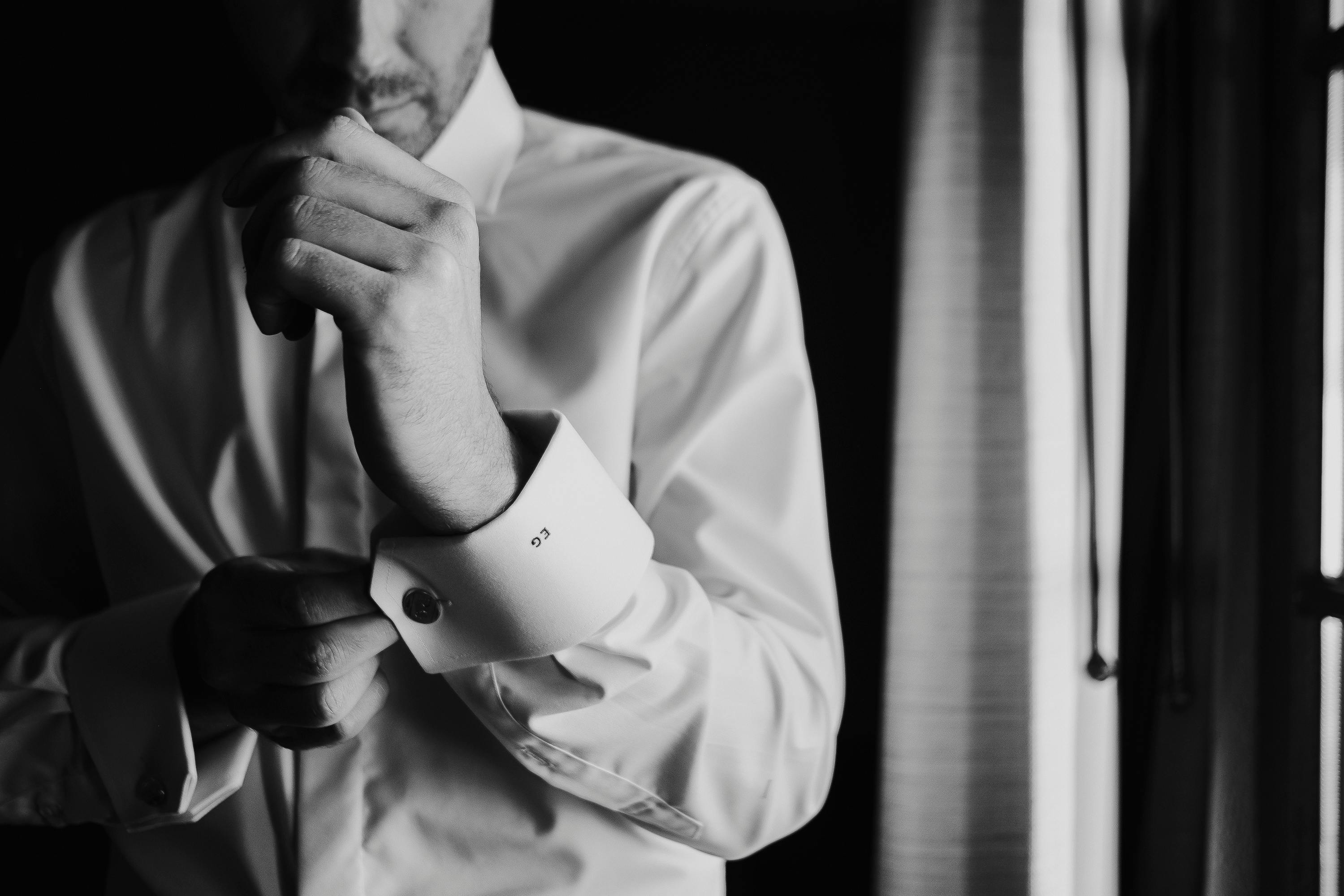 A groom adjusts his cufflinks in a black and white portrait, capturing wedding day elegance.