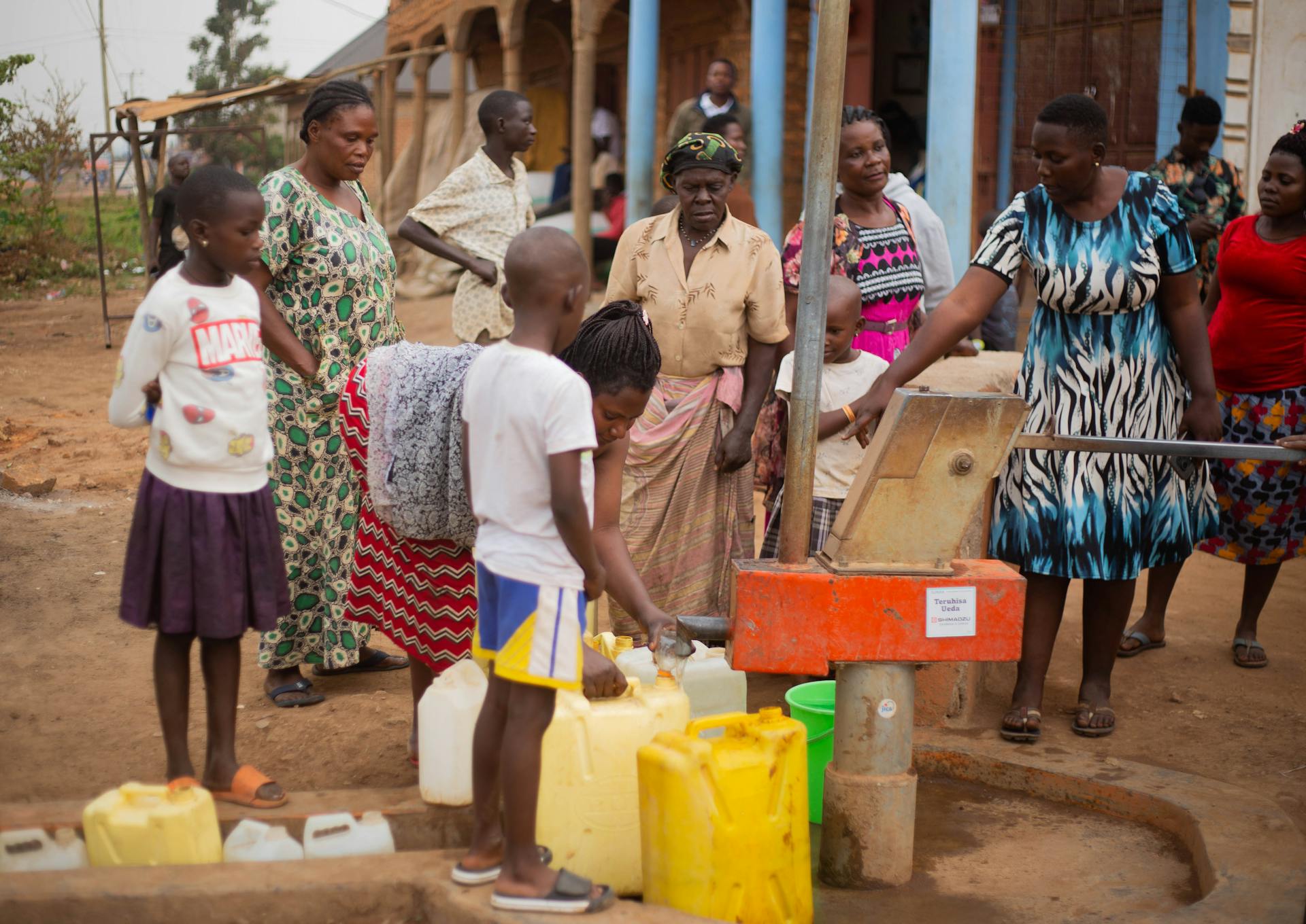 Women and children collect water from a pump in a rural village setting.