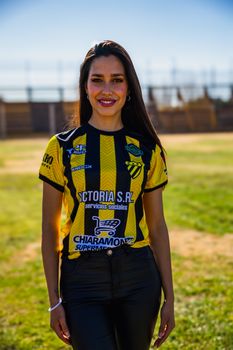Smiling woman in a black and yellow sports jersey standing on a sunny field.