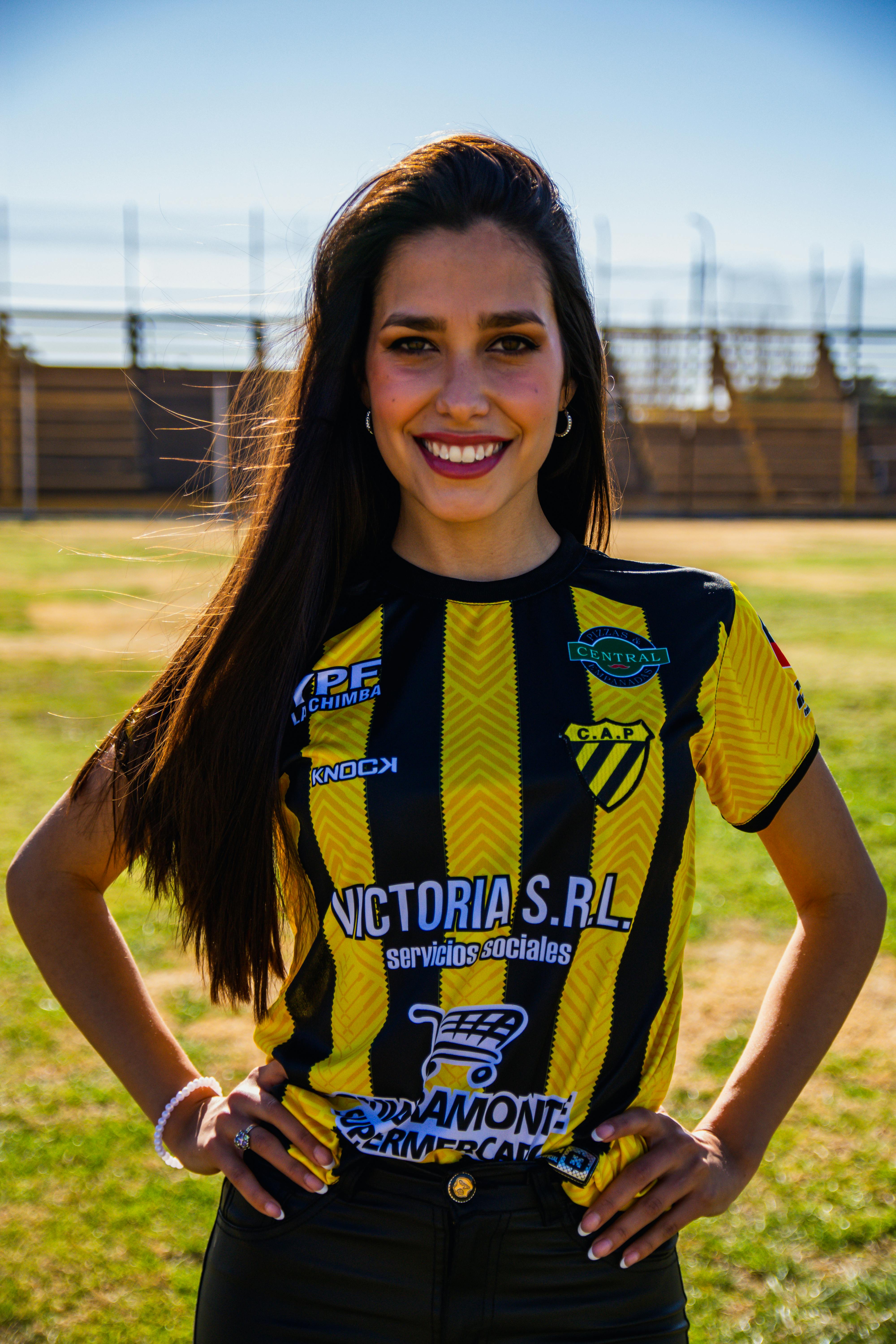 Young woman smiling confidently in a black and yellow soccer jersey outdoors.