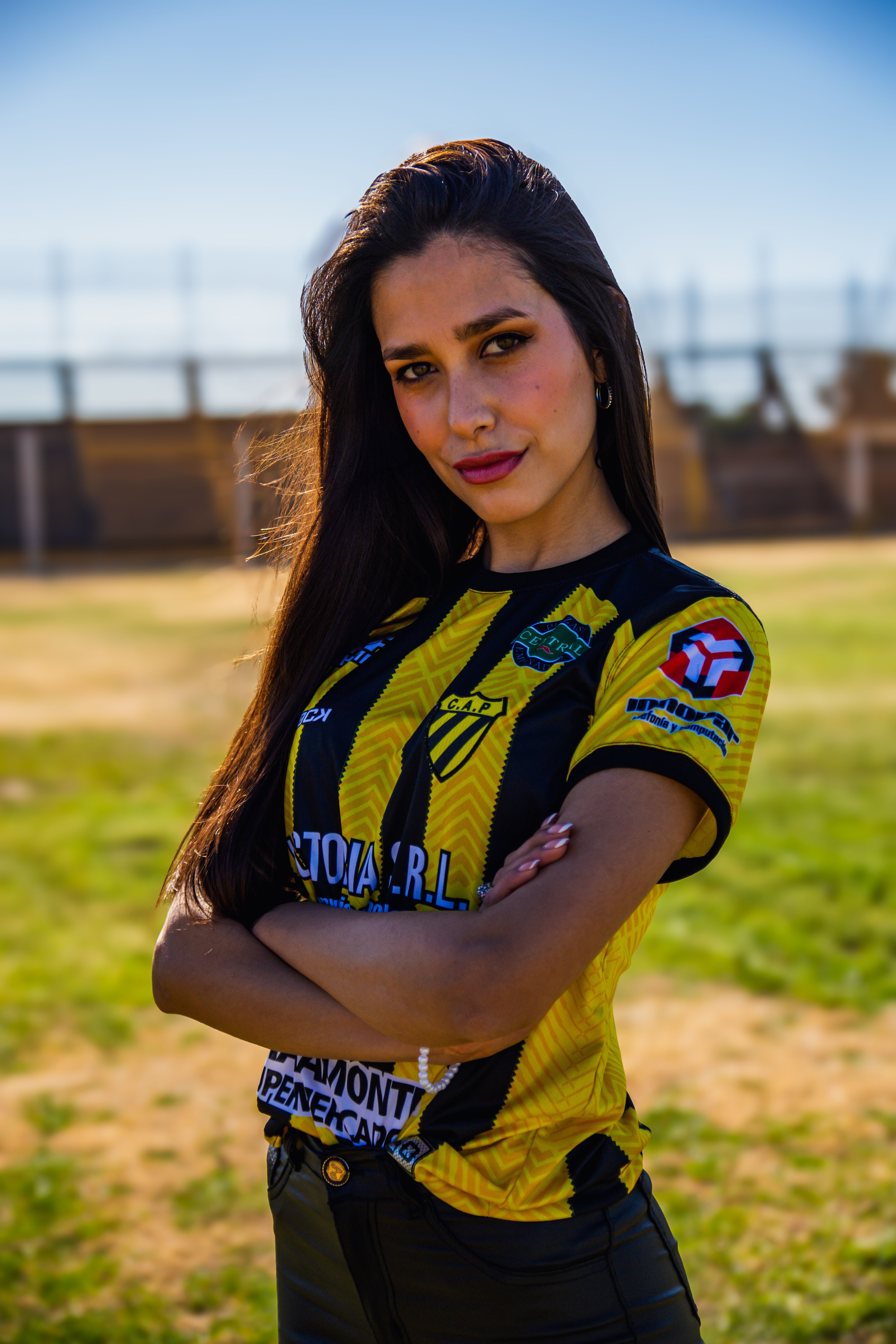 Young woman posing confidently in a sports jersey outdoors on a sunny day.