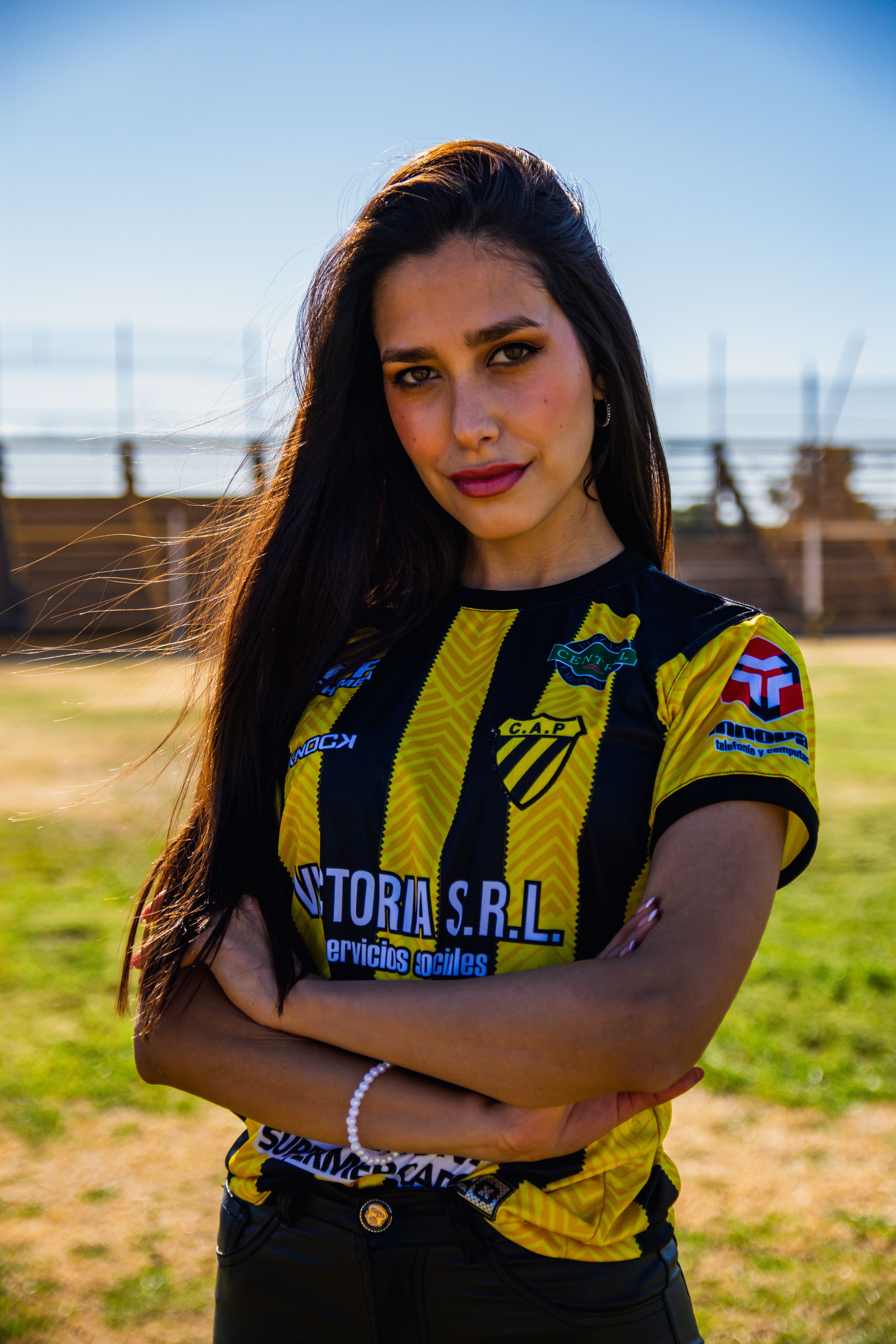 A young woman posing confidently in a sports jersey at an outdoor stadium.