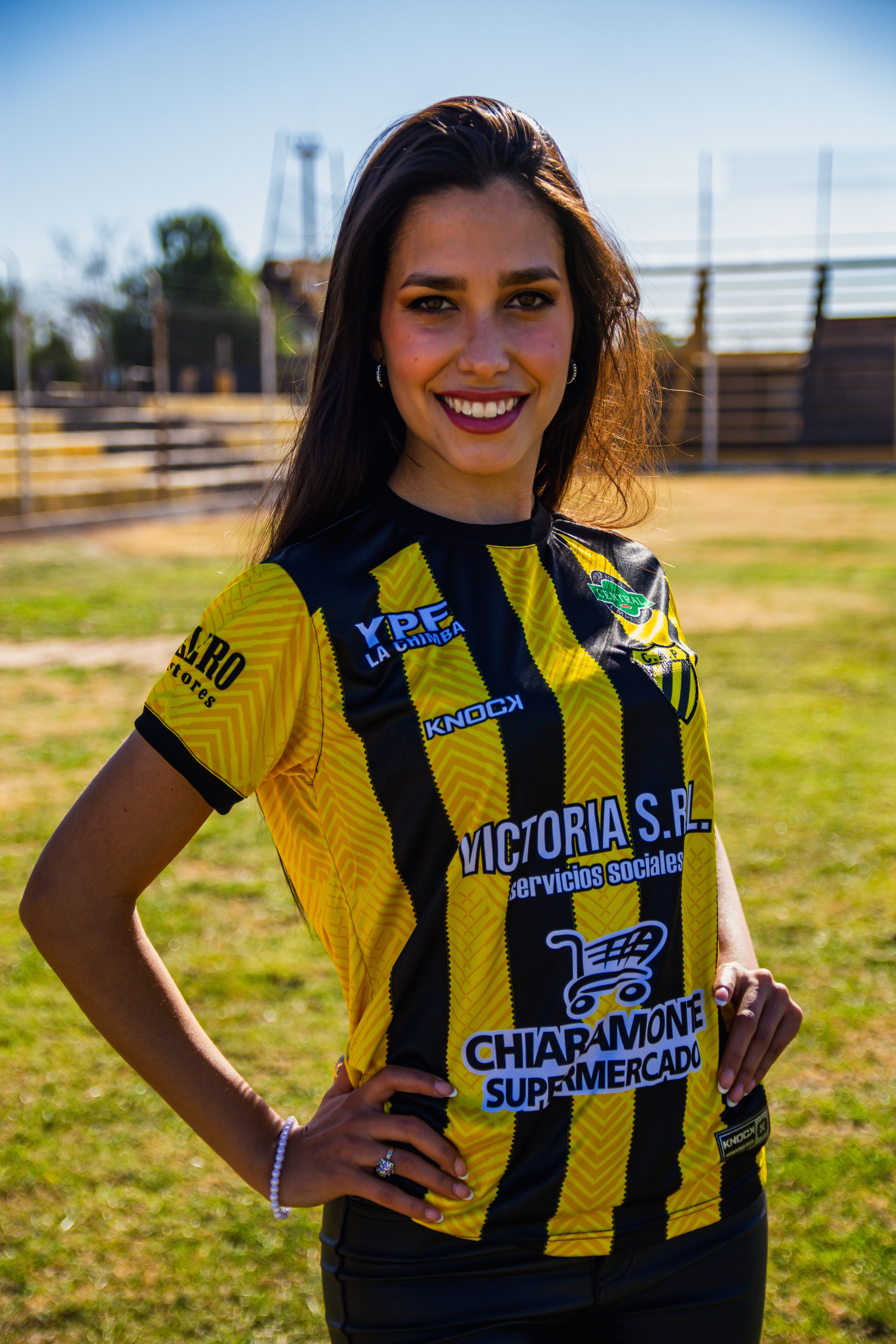 Energetic young woman in yellow soccer jersey smiling outdoors on a sunny day.