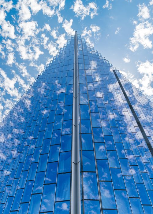 Free Modern skyscraper with glass facade reflecting clouds, against a bright blue sky, symbolizing contemporary urban architecture. Stock Photo