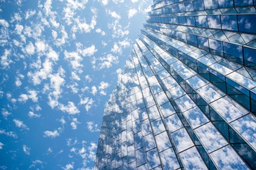 Free A contemporary skyscraper with glass windows reflects a bright blue sky filled with clouds. Stock Photo