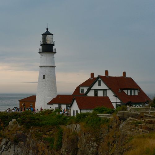 Free A picturesque lighthouse on a rocky coast with adjacent buildings under a serene sky. Stock Photo