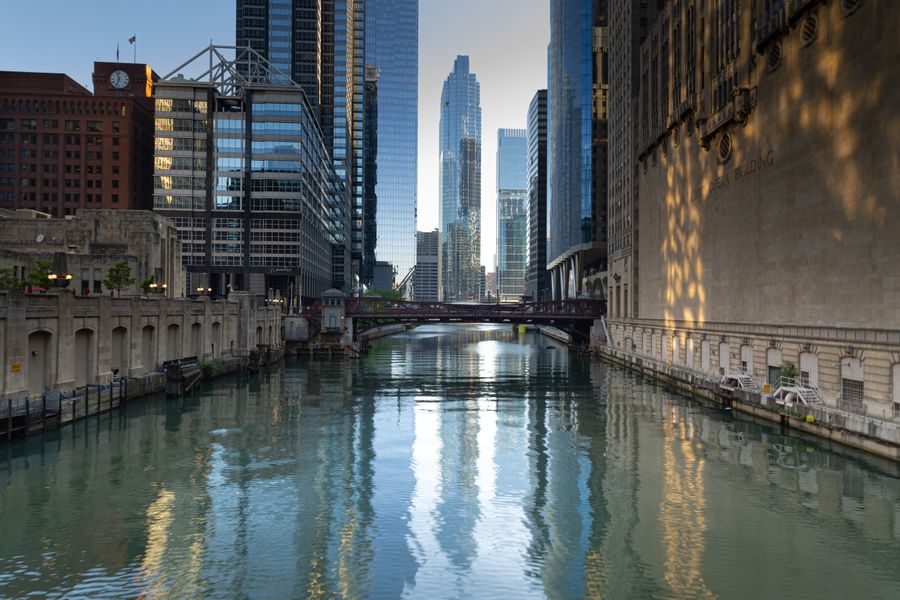 Chicago River lined with historic and modern buildings under blue sky with reflections in calm water
