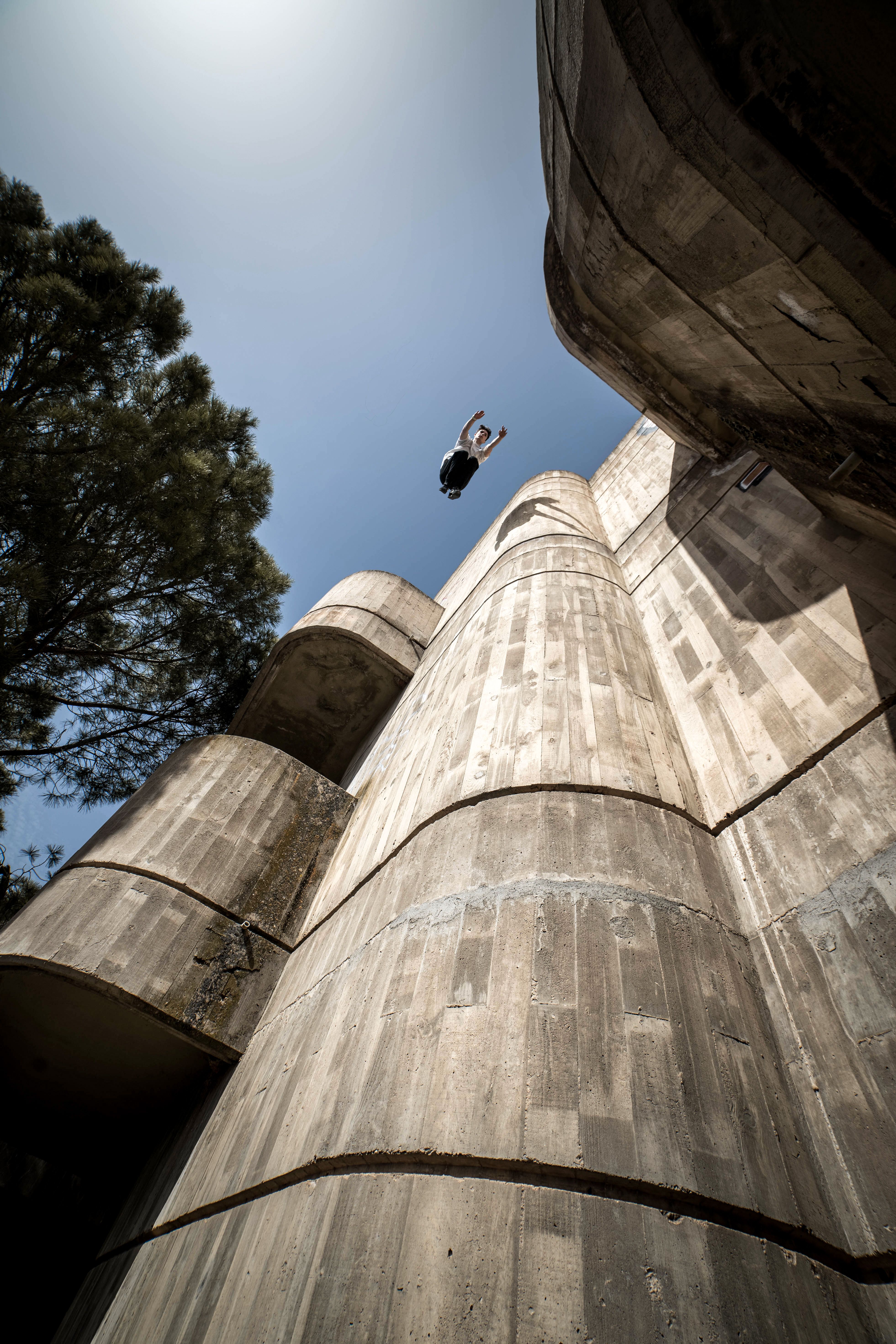 A person performing a parkour jump off a building into the clear sky.