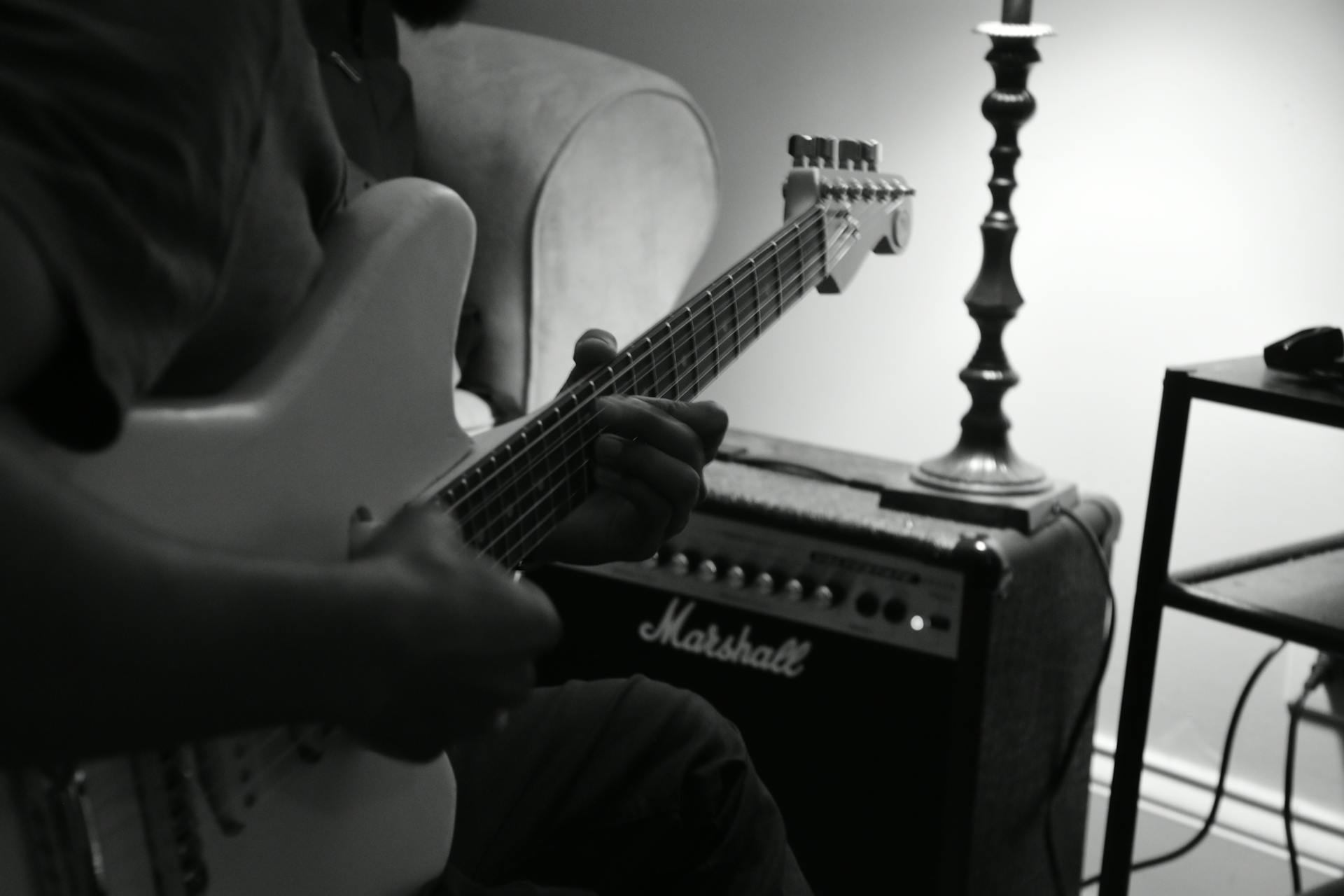 Black and white image of a guitarist playing electric guitar next to a Marshall amplifier indoors.