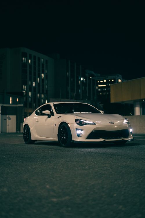 Free A stylish white car parked in a cityscape at night, showcasing urban elegance and automotive design. Stock Photo