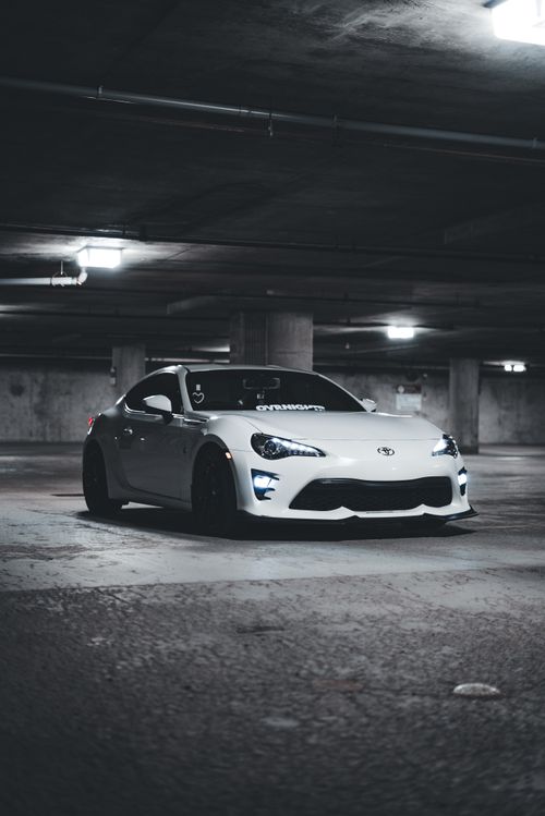 Free White sports car parked in dimly lit underground garage, capturing luxury automotive elegance. Stock Photo