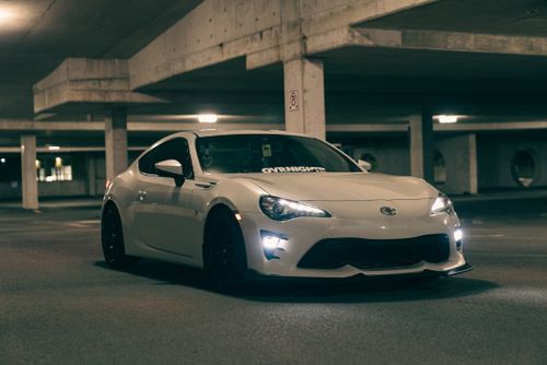 Free A stylish white coupe parked in a dimly lit parking garage at night. Stock Photo