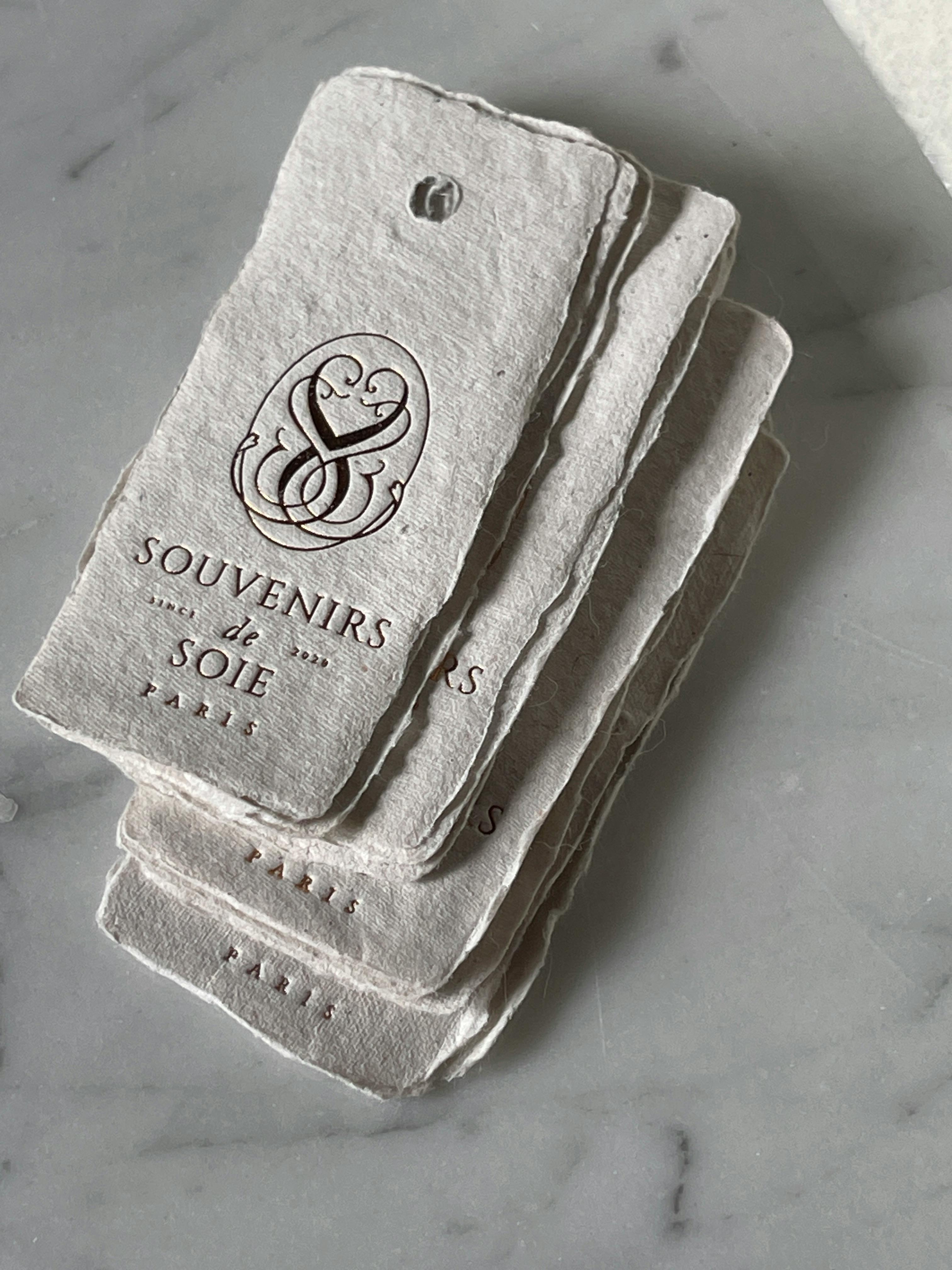 Stack of vintage-style Souvenirs de Soie Paris tags on a marble surface.