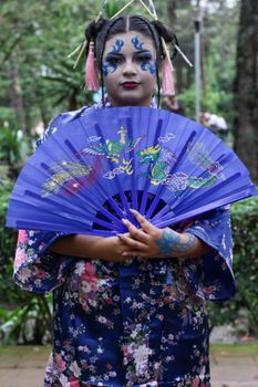 A striking portrait of a woman in traditional costume holding a decorative fan in a garden.