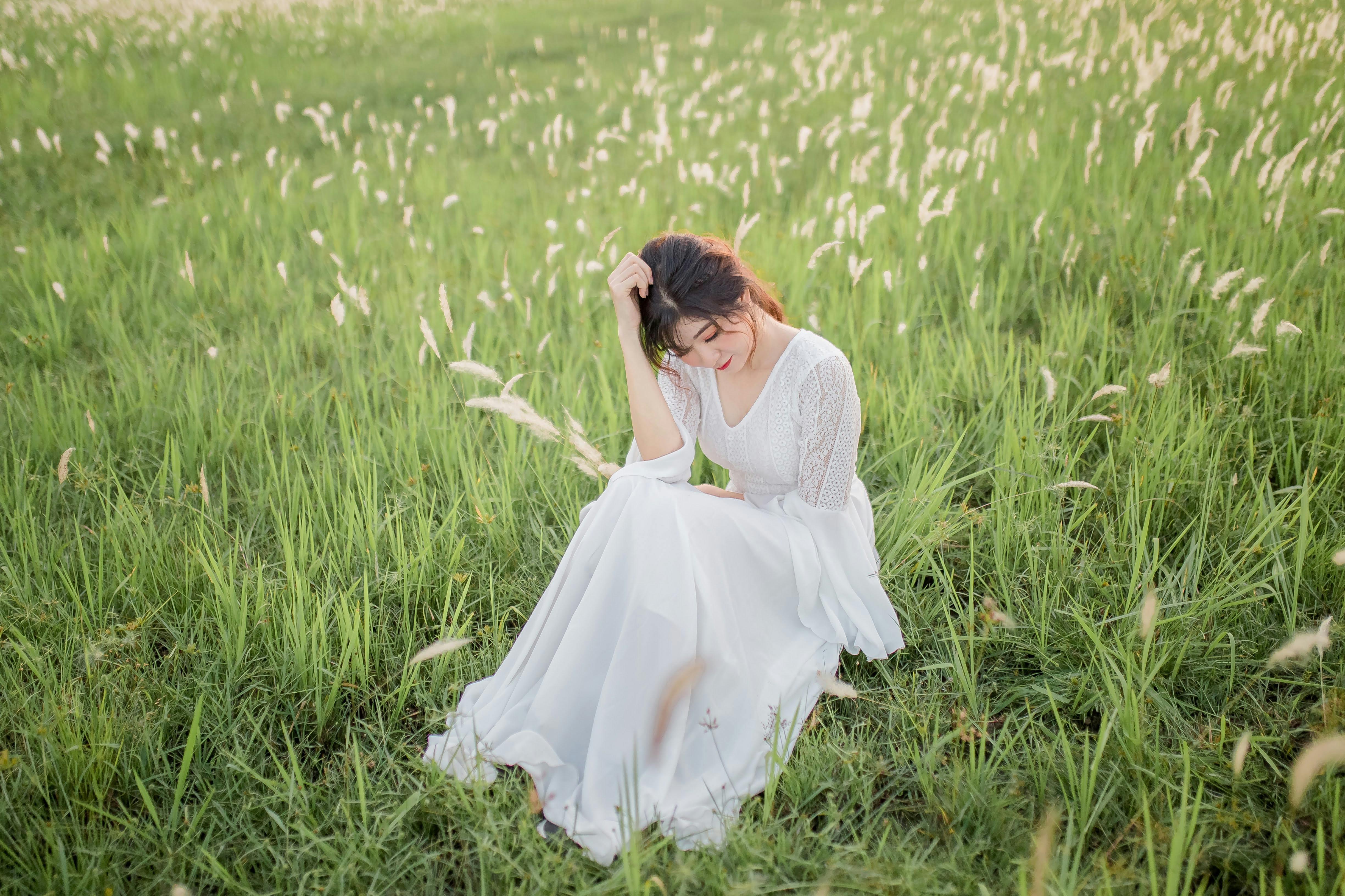 Asian woman in a white dress sitting in a green meadow with tranquility.