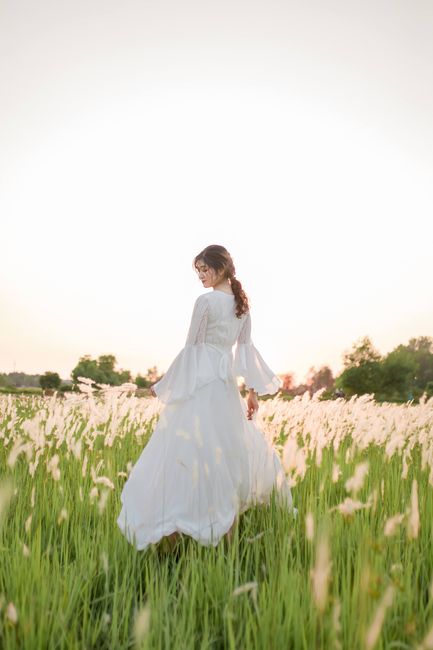 A woman in a flowing white dress stands in a serene field at sunset, evoking tranquility.