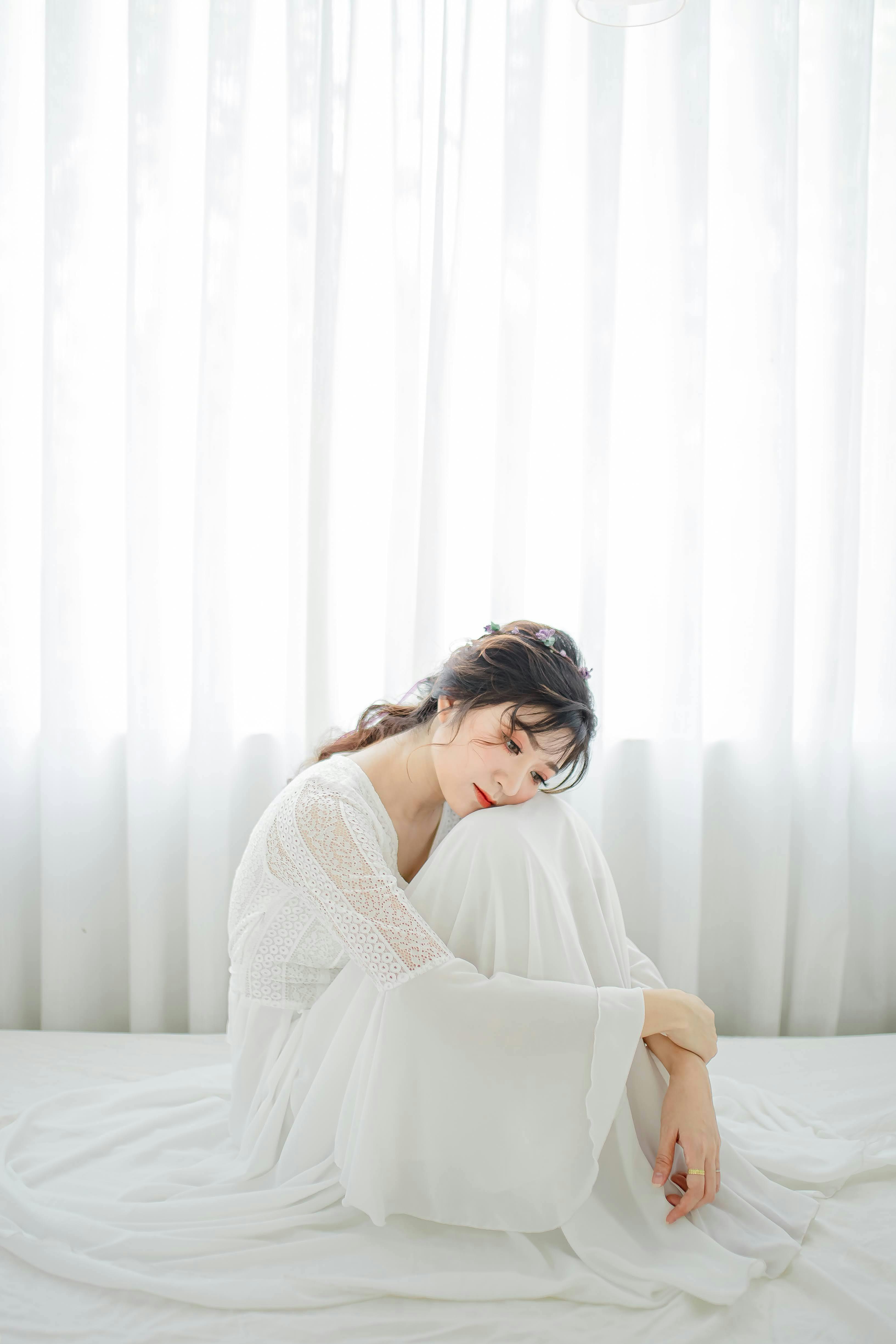 Graceful woman in white dress sitting serenely by the window, capturing soft daylight.