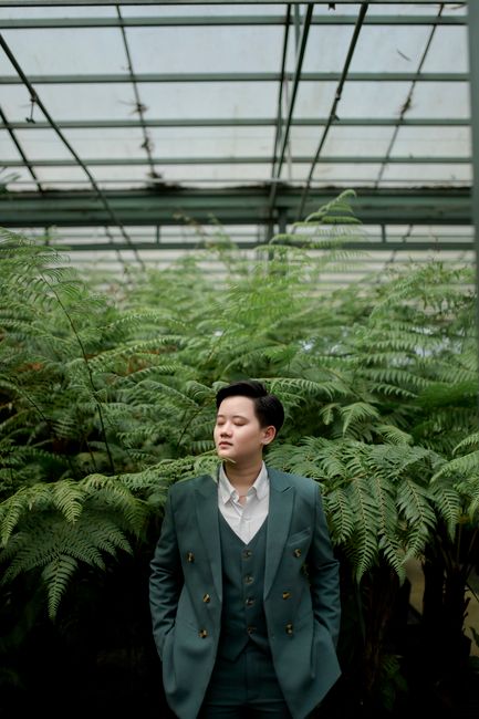 Elegant portrait of an Asian woman in a suit surrounded by lush ferns inside a greenhouse.