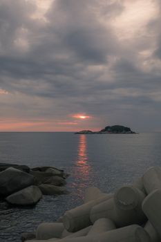 Serene seascape featuring a tranquil sunset over the ocean with scattered rocks and calm waters.