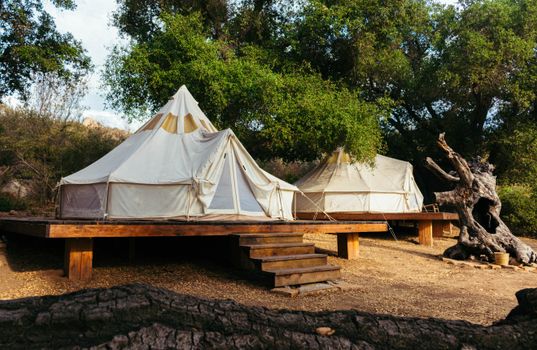Two spacious canvas tents on a wooden platform in a serene forest setting, ideal for a summer escape.