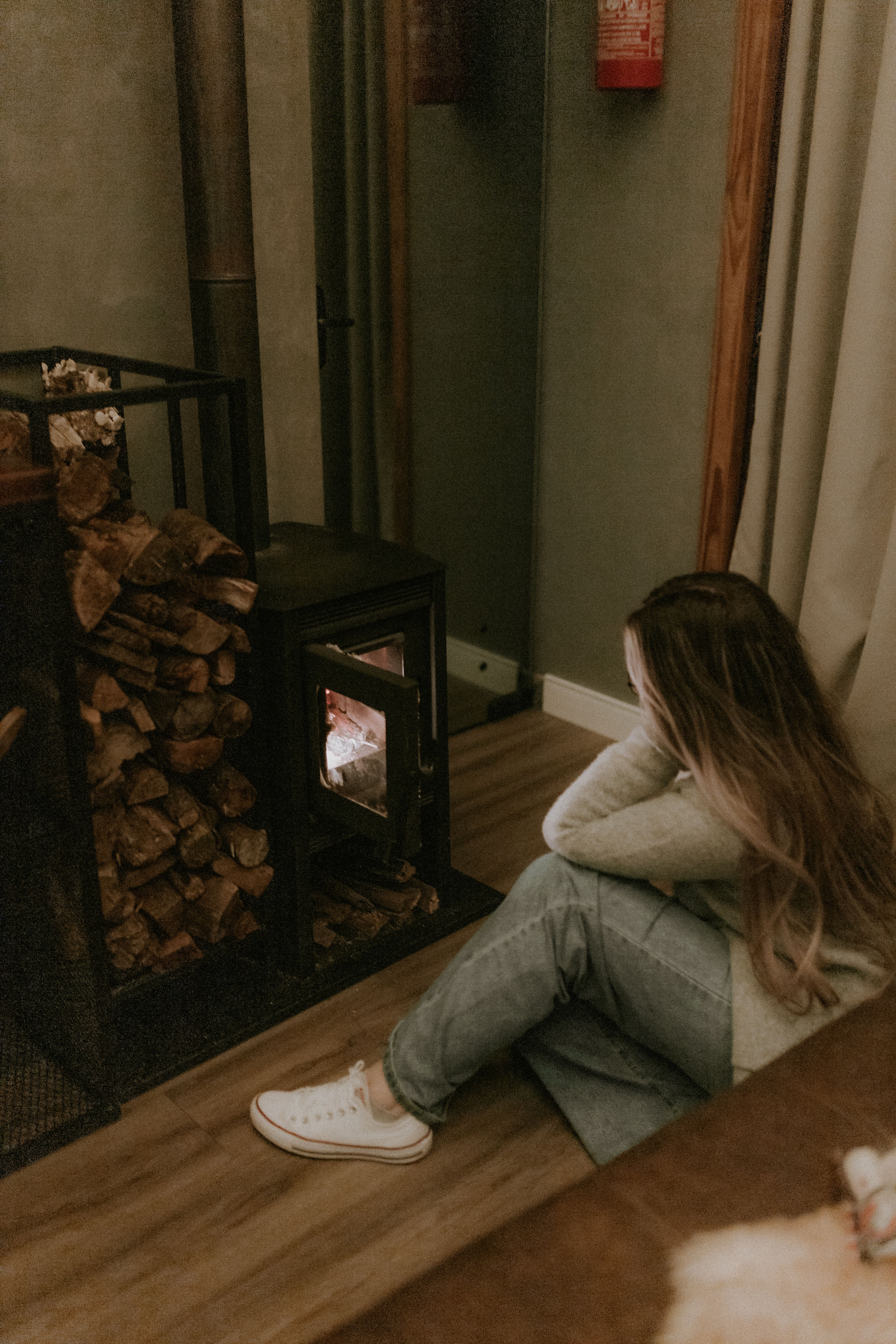 A woman sitting by a lit wood-burning stove