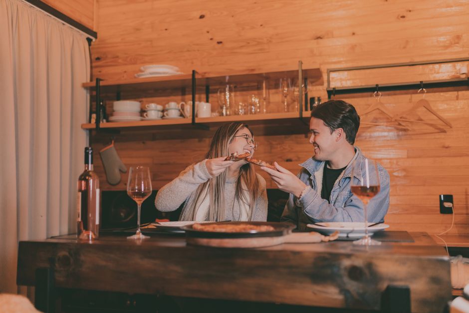 A couple enjoying pizza and wine at a rustic wooden table in a cozy setting.