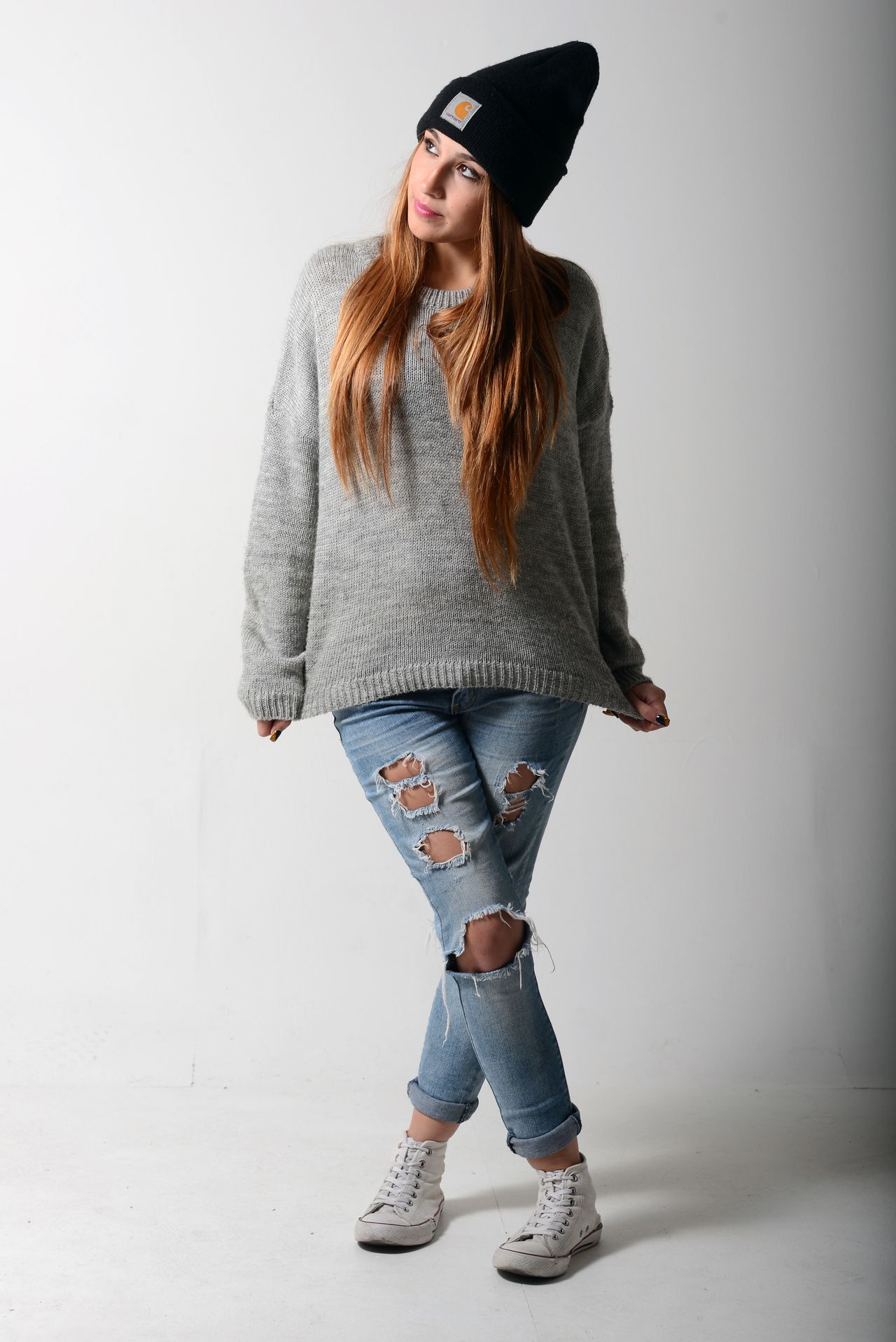 Young woman in a black beanie, gray sweater and ripped jeans