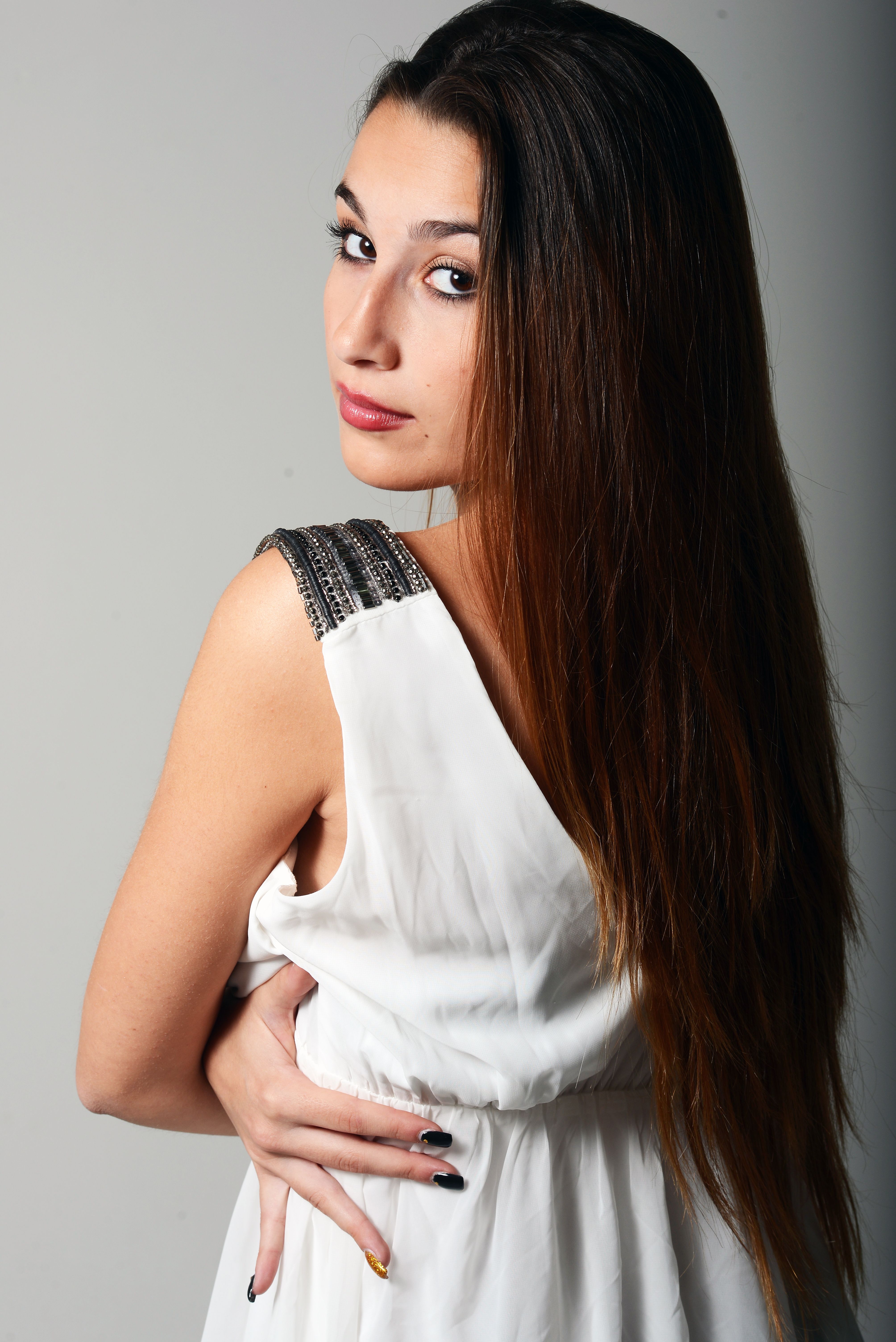 Portrait of a young woman with long hair in a stylish white dress, posing gracefully indoors.