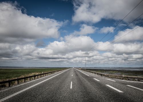 Free A scenic view of a straight road on Rømø Island, Denmark with dramatic clouds and coastal landscape. Stock Photo