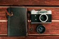 木桌上放着一台经典的复古相机和一本皮革日记本，唤起了怀旧与冒险的情怀