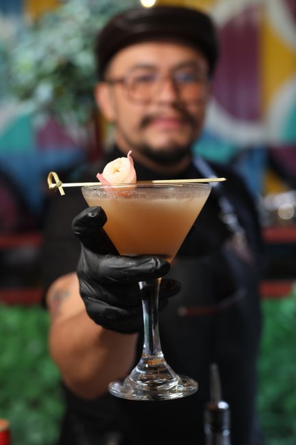 A pale pink lychee martini in a chilled martini glass, garnished with a peeled lychee fruit speared on a cocktail pick and beads of condensation on the glass.