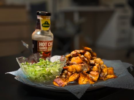 Delicious roasted potatoes paired with hot sauce and fresh salad indoors.