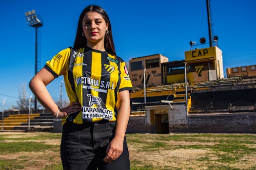 Confident woman posing in a soccer jersey in an outdoor sports field.