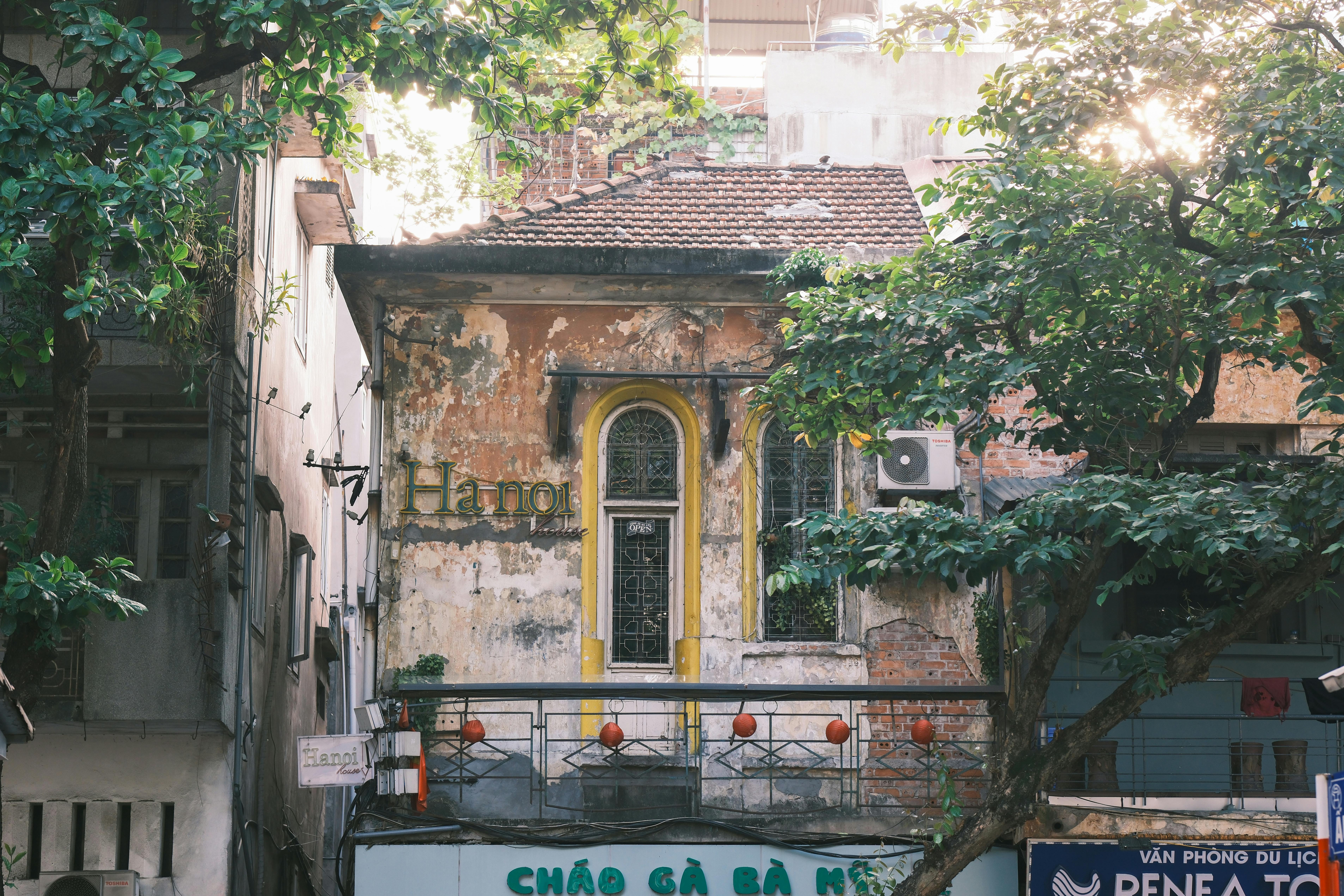 A vintage building in Hanoi surrounded by lush foliage and urban elements, showcasing traditional architecture.