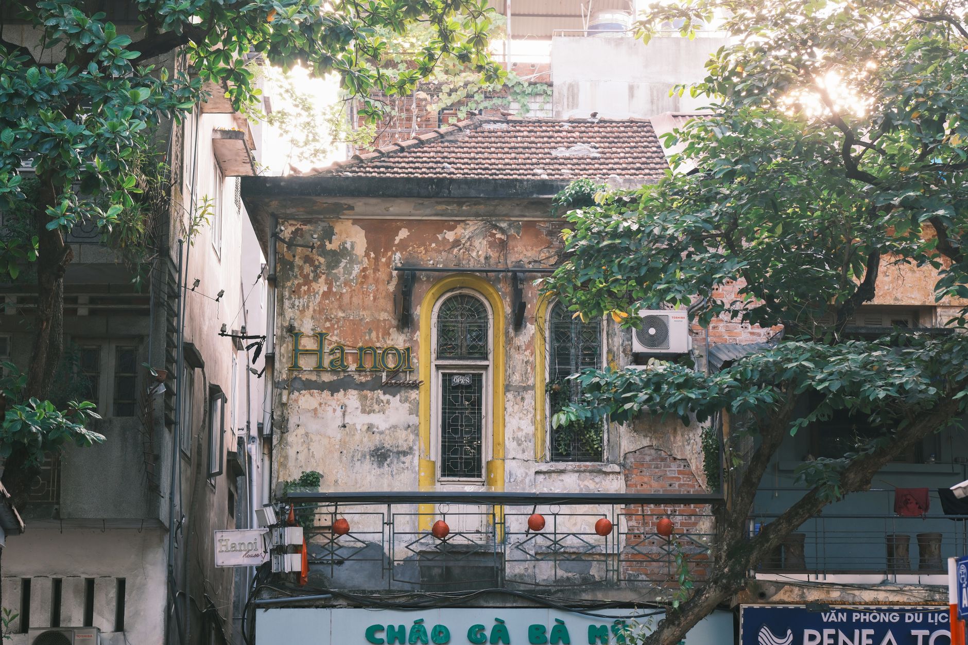 A vintage building in Hanoi surrounded by lush foliage and urban elements, showcasing traditional architecture.