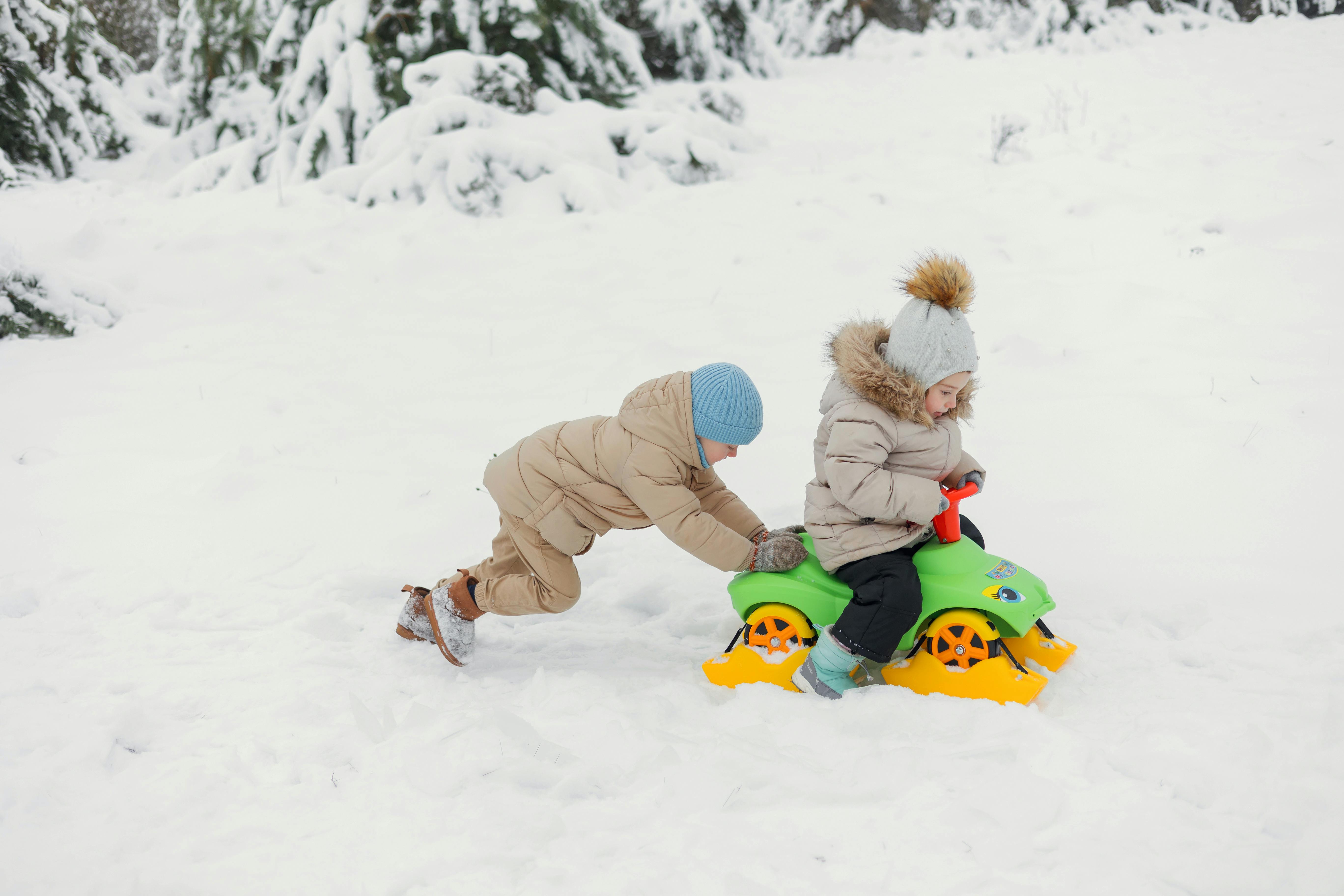 child pushing a friend on the snow runner