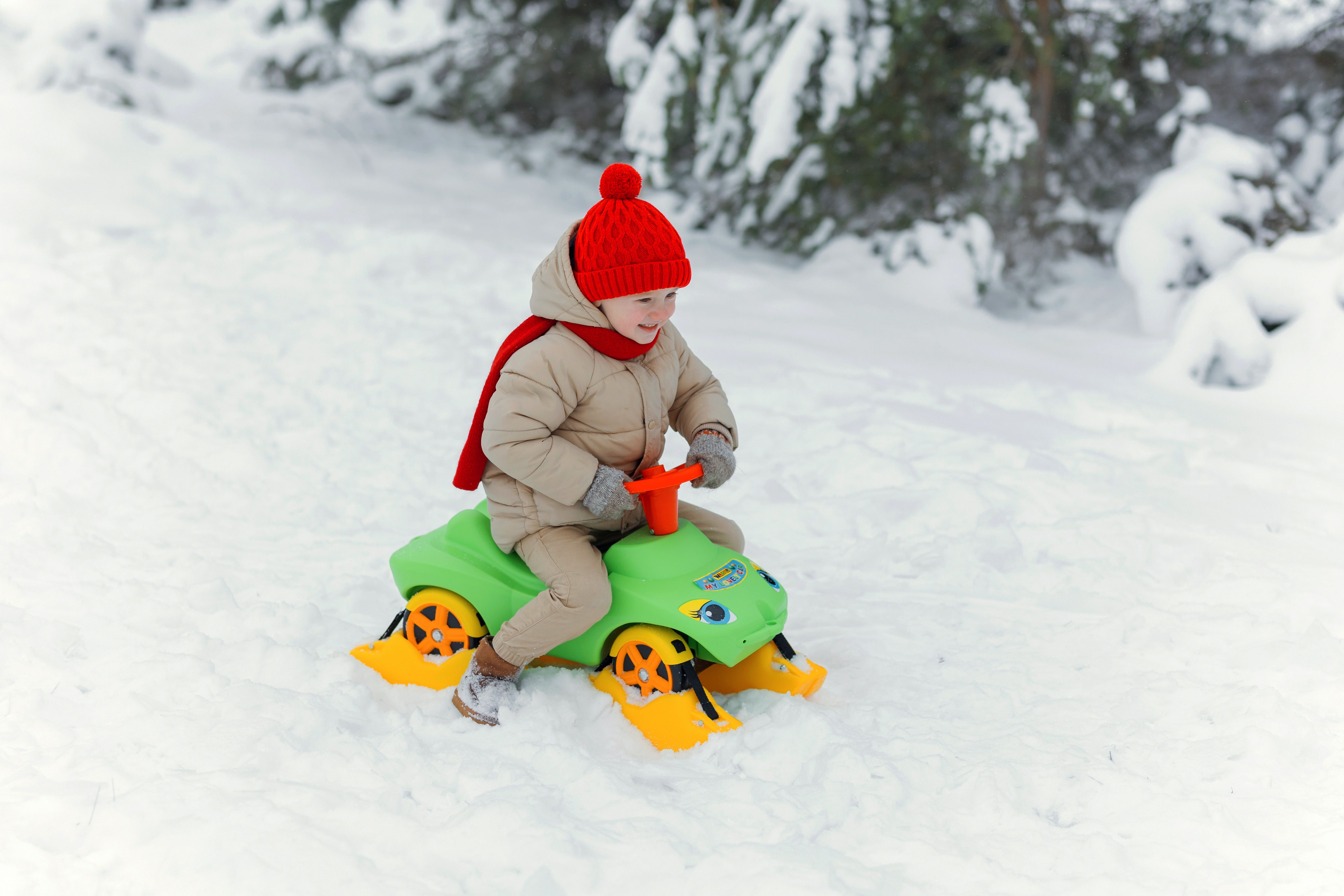 Young child having fun riding a snow toy in a winter wonderland, dressed warmly in a red hat and scarf.