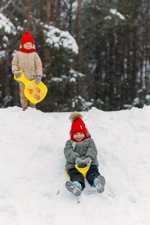 Free Two children enjoying a snowy day, sledding down a hill in winter attire. Stock Photo