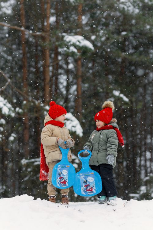 Free Two kids in winter clothes playing with sleds in a snowy forest setting. Stock Photo