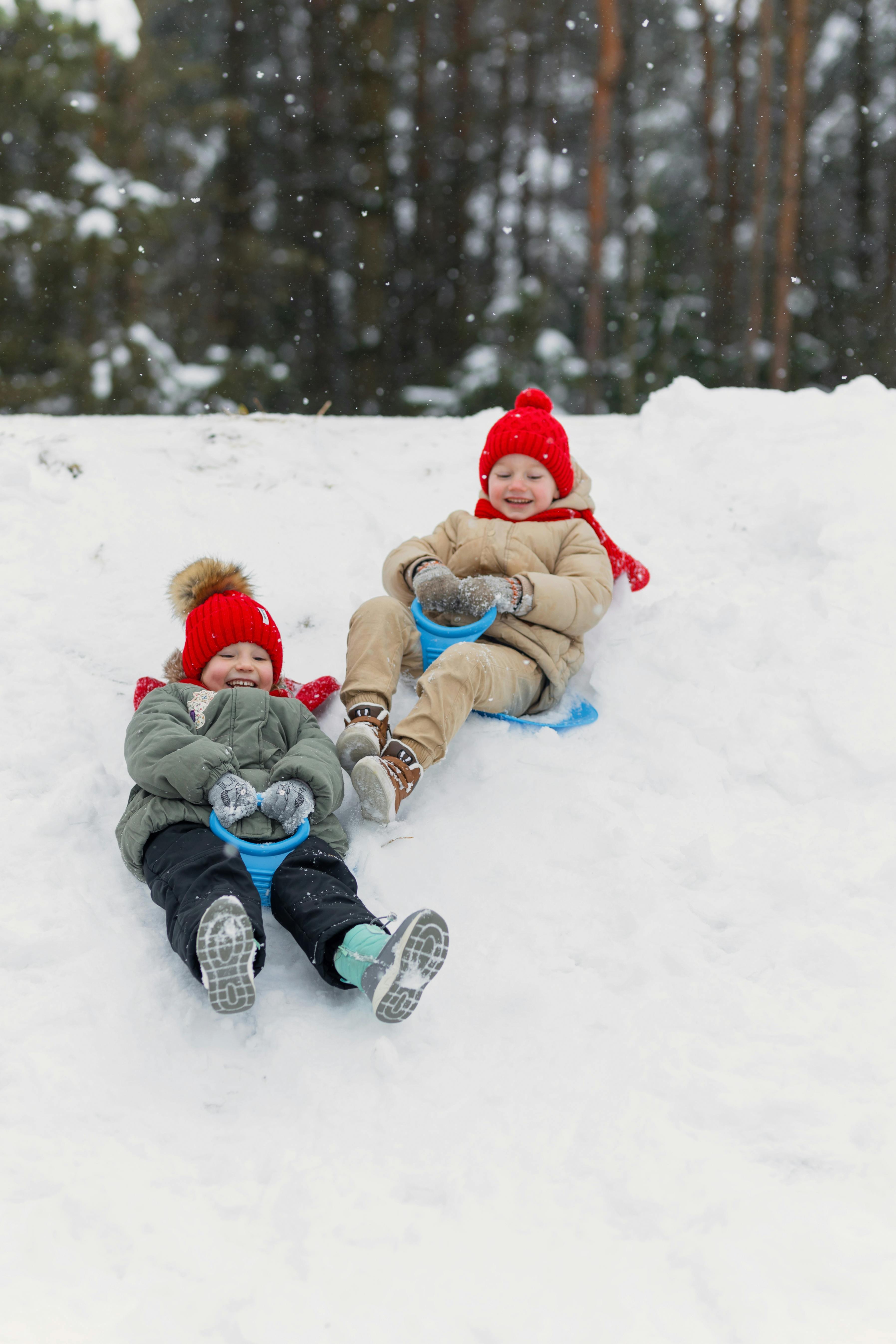 siblings sliding down a snowy hill