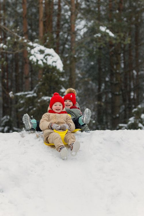 Free Two joyful children sledding down a snowy hill, enjoying a winter day outdoors. Stock Photo