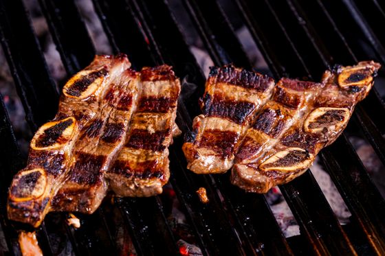Two strips of cross-cut beef short ribs with charred bone rounds sizzling on a charcoal grill