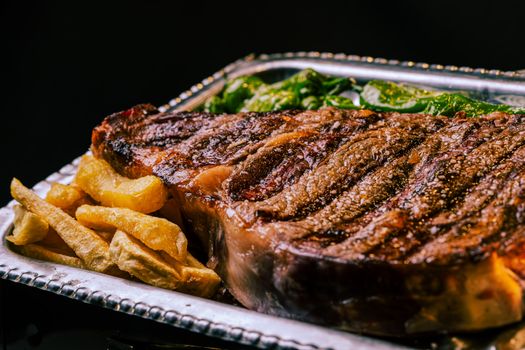 Close-up of a delicious grilled steak with crispy fries and fresh greens on a platter.