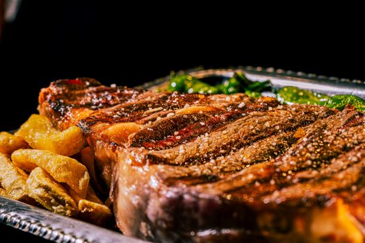 Close-up of a juicy grilled ribeye steak with pepper and sides on a silver platter.