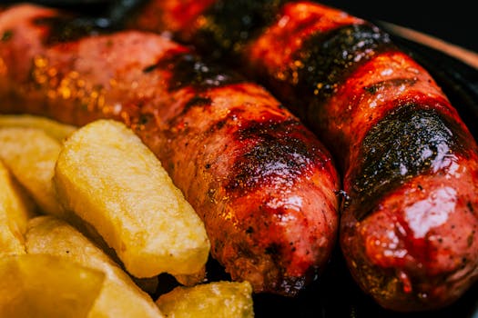 Close-up of perfectly grilled sausages and golden potato wedges. Ideal for barbecue lovers.