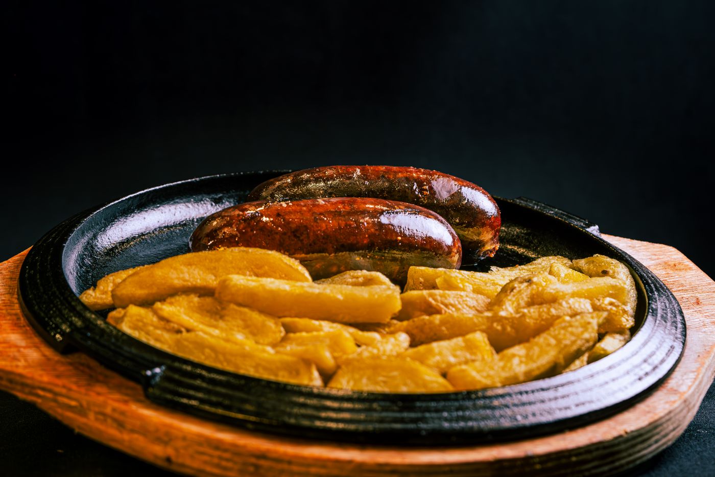 Rustic grilled sausage and potatoes served hot on a wooden sizzling plate, perfect for a hearty meal.