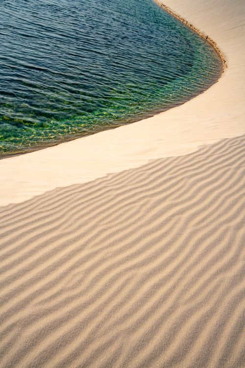 Free Tranquil coastal view of rippled sand dunes meeting the clear blue sea under a sunny sky. Stock Photo
