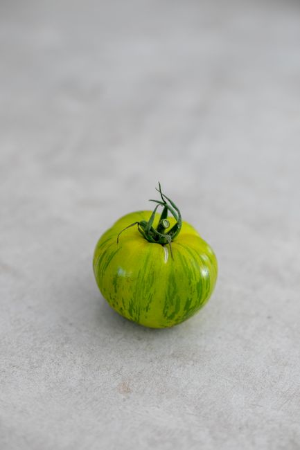 A close-up shot of a single vibrant green heirloom tomato on a soft, neutral background.