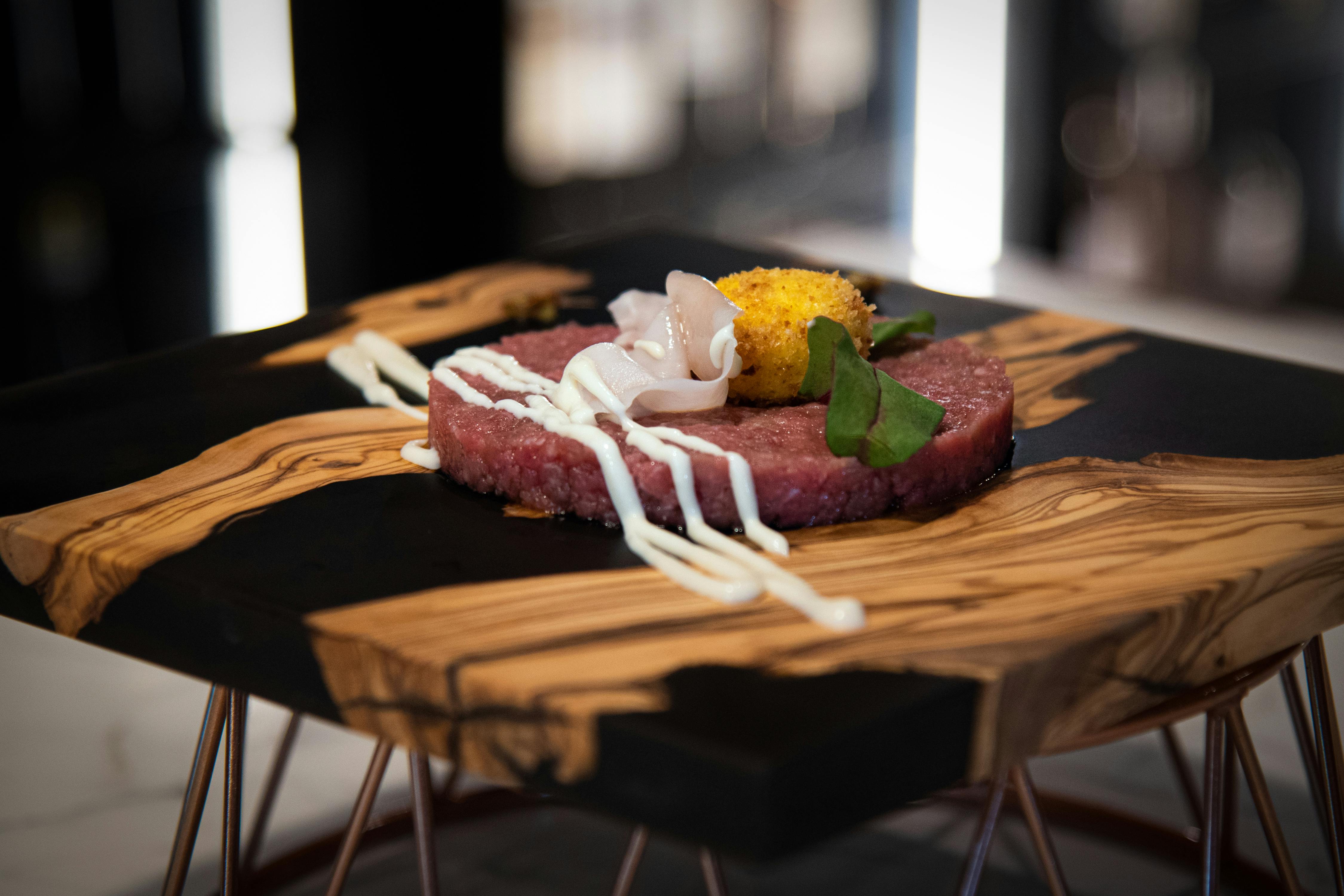 A gourmet beef tartare elegantly presented with artistic garnishments on a wooden platter.